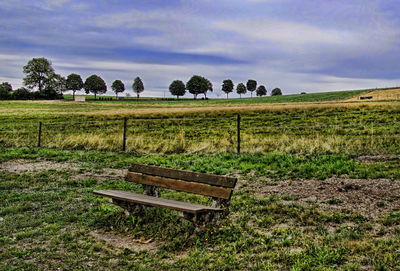 Empty bench on field against sky