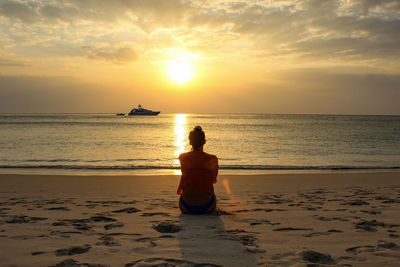 Rear view of man sitting on beach during sunset