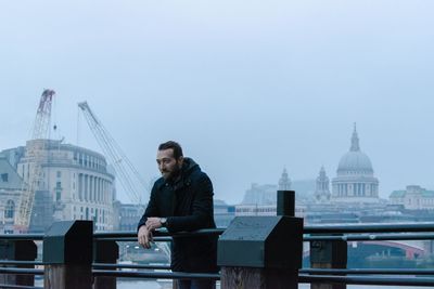 Man leaning on railing against buildings in city