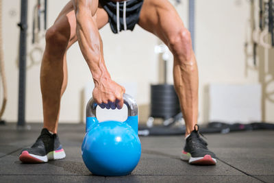 Low section of man holding kettlebell on floor in gym