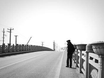Woman standing on railing of bridge against clear sky