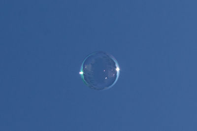 Low angle view of bubbles against clear blue sky