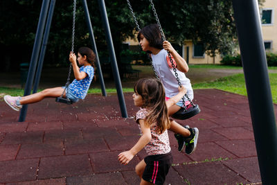 Three girls playing at children playground with swings in public park
