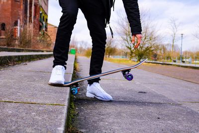 Low section of man skateboarding on footpath against sky