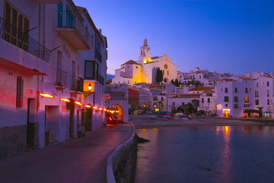 Illuminated buildings by street against sky at dusk