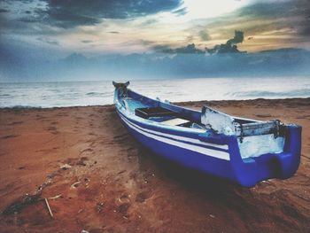 Boat moored on beach against sky during sunset