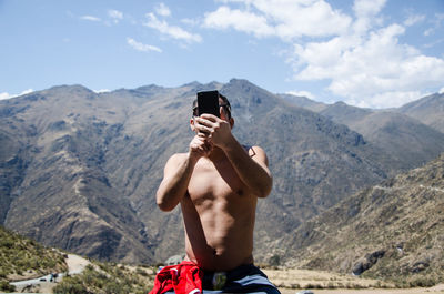 Shirtless man using mobile phone against mountains and sky