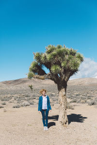 Young woman standing on desert against clear blue sky