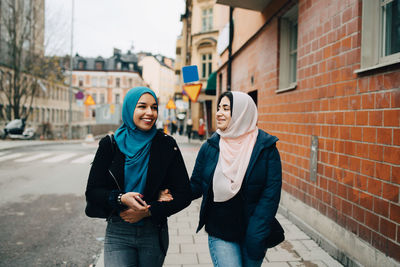 Happy female muslim friends walking on sidewalk in city