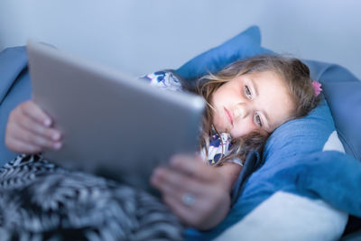 Cute girl using digital tablet while lying on bed at home
