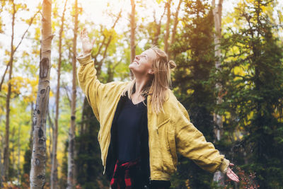 Young woman looking away while standing on tree in forest