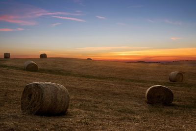 Hay bales on field against sky at sunset