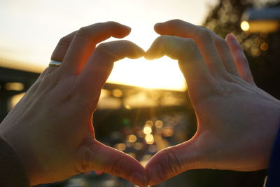 Cropped hands making heart shape against sky