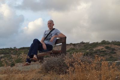 Side view of man siting on mountain against sky