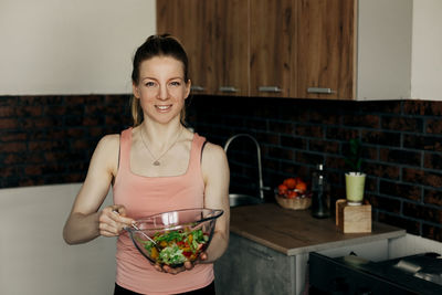 Portrait of an attractive woman holding a salad bowl and looking at the camera.