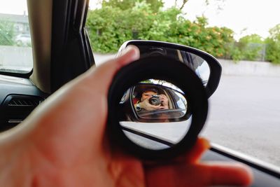 Reflection of man photographing camera on side-view mirror