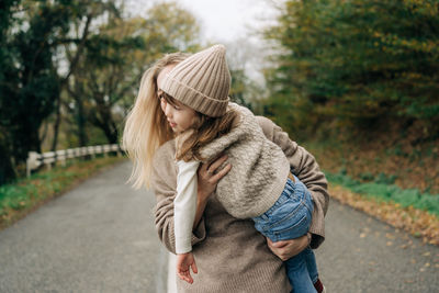 Mom has fun with her little daughter hugging and holding her in her arms on a country road.