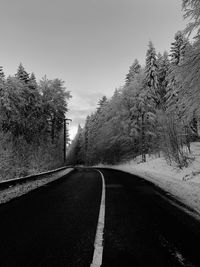 Empty road along trees and against sky