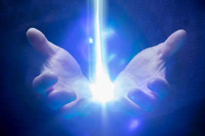 Digital composite image of hand against illuminated blue light