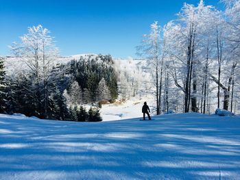 Person on snow covered landscape against blue sky