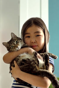 Child portrait with domestic pet, cute asian girl holding tabby cat