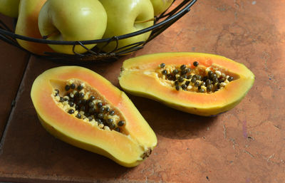 High angle view of halved papaya by granny smith apples in container on table