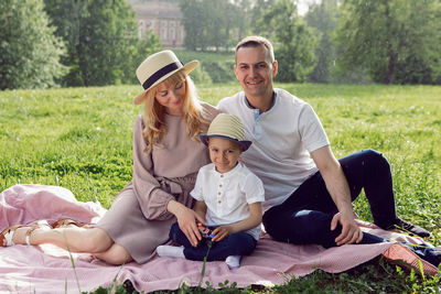 Family with a child a boy of 4 years old. with a car toy sitting on a green field under a tree