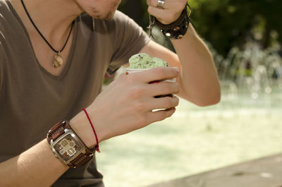 Midsection of young man having ice cream by fountain in park