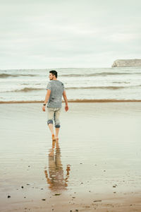 Rear view of mid adult man standing at beach against sky