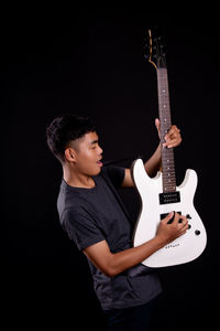 Young man playing guitar against black background