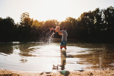 Father holding young child in the air at the lake splashing water