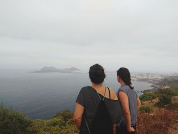 Rear view of women standing on mountain against sea and sky