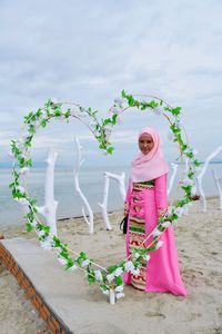 Woman standing by pink flowers against sky