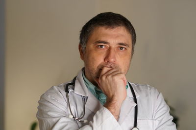 Portrait of thoughtful mature doctor against wall