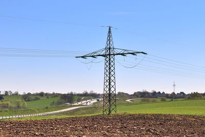Electricity pylons on field against clear sky