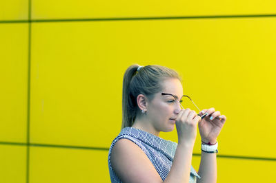 Woman wearing eyeglasses by yellow wall