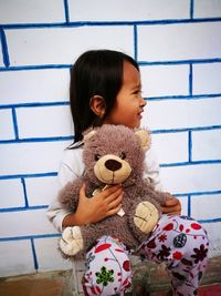 Cute girl sitting with teddy bear against wall