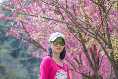 Close-up of young woman standing by pink flowers in park