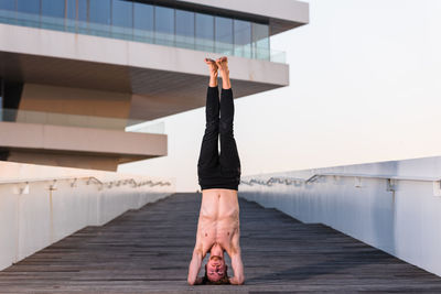 Full length of shirtless man doing headstand against building