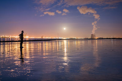 Man standing at beach against sky at dusk
