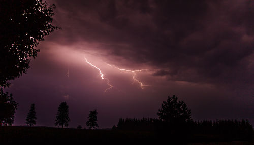 Lightning over silhouette trees against dramatic sky at night