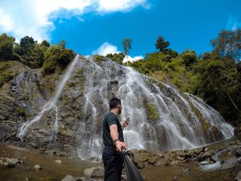 Man using mobile phone against waterfall