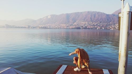 Woman crouching on pier over lake against sky