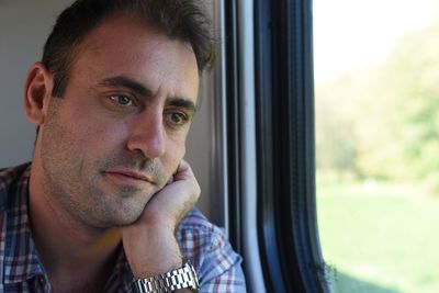 Close-up of thoughtful mid adult man looking through window in train