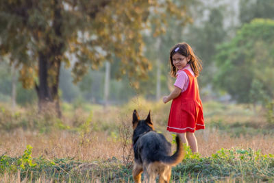 Cute girl looking at dog on field