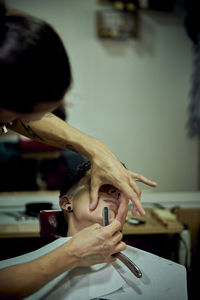 A barber is shaving a young boy with a razor