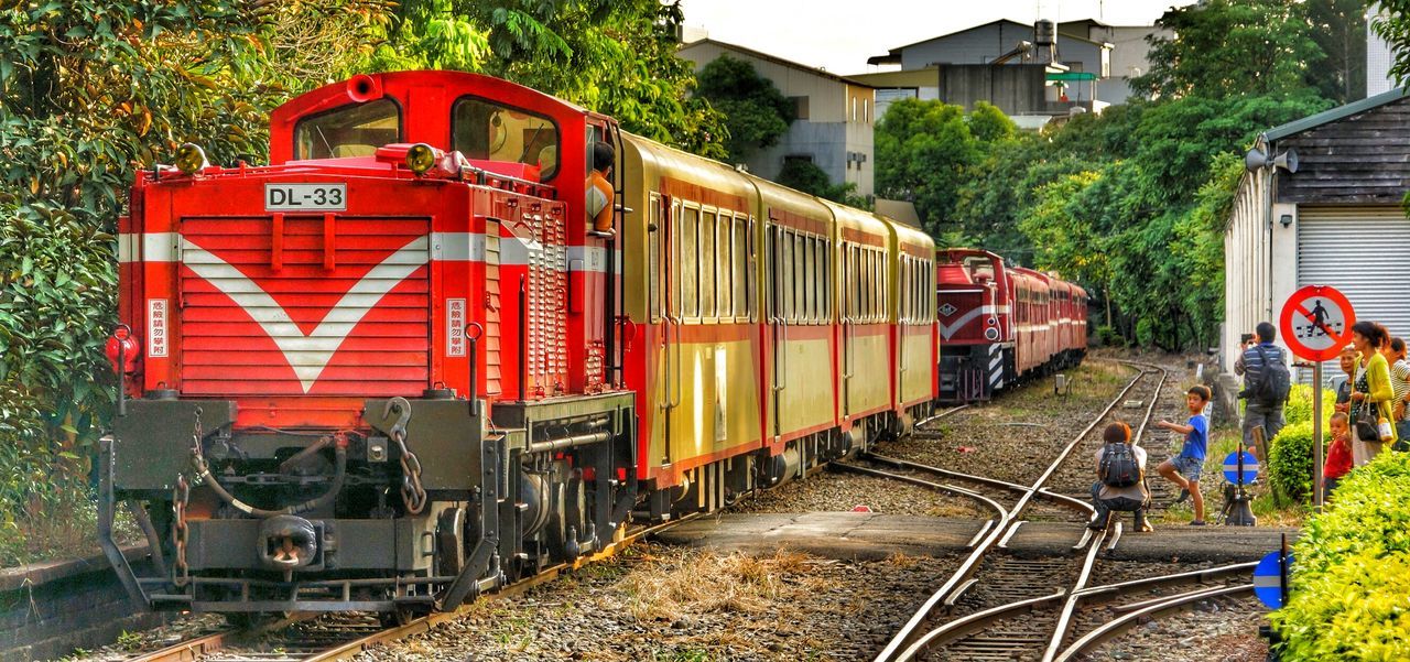 transportation, railroad track, mode of transport, rail transportation, public transportation, red, land vehicle, tree, train - vehicle, travel, building exterior, day, built structure, outdoors, incidental people, architecture, railroad station, the way forward, stationary, in a row