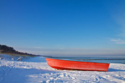 Red boat on sea shore against clear blue sky