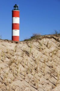 Lighthouse by mountain against clear blue sky