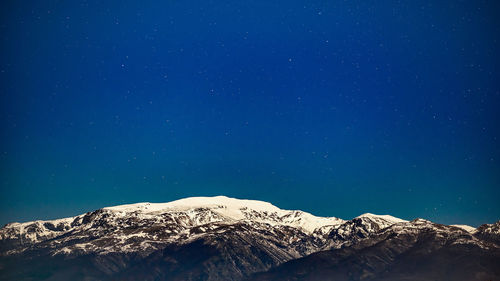 Low angle view of snowcapped mountain against blue sky